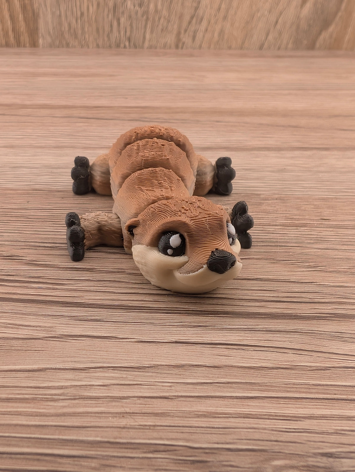 Textured brown segmented otter figurine relaxing on wood, head toward camera with four splayed black multi-jointed feet.
