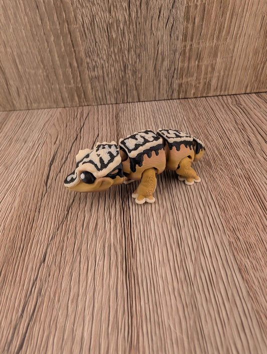 Segmented beige and brown reptile figure with bold black and white markings, posed on a rustic wooden floor texture.