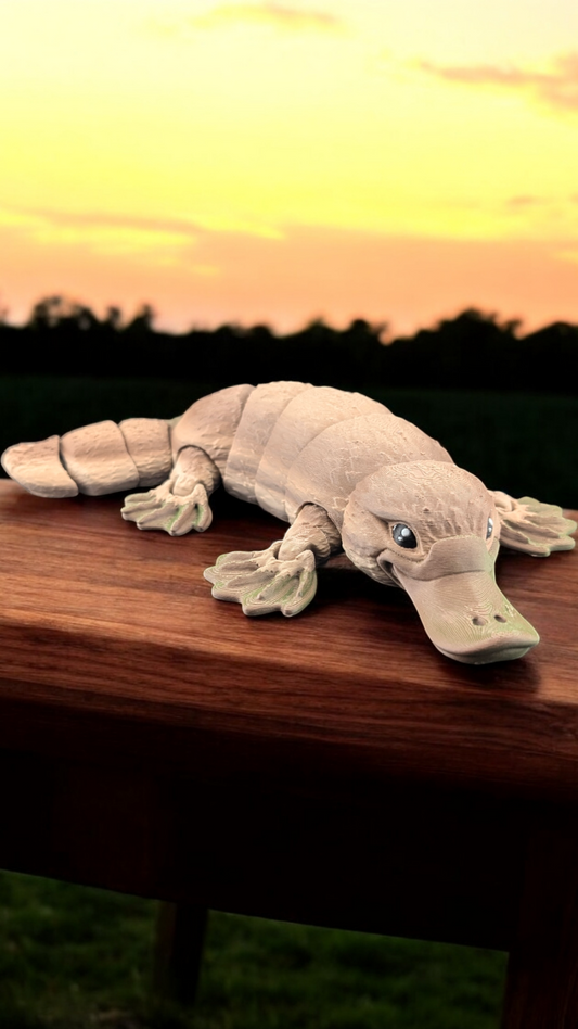 Flexible tan platypus toy rests on a wooden railing at sunset, showing its segmented body and green beak.