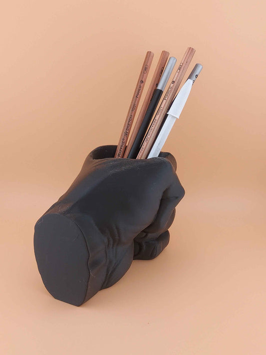 Solid black fist container holding an assortment of light wood, charcoal, and white drawing pencils.
