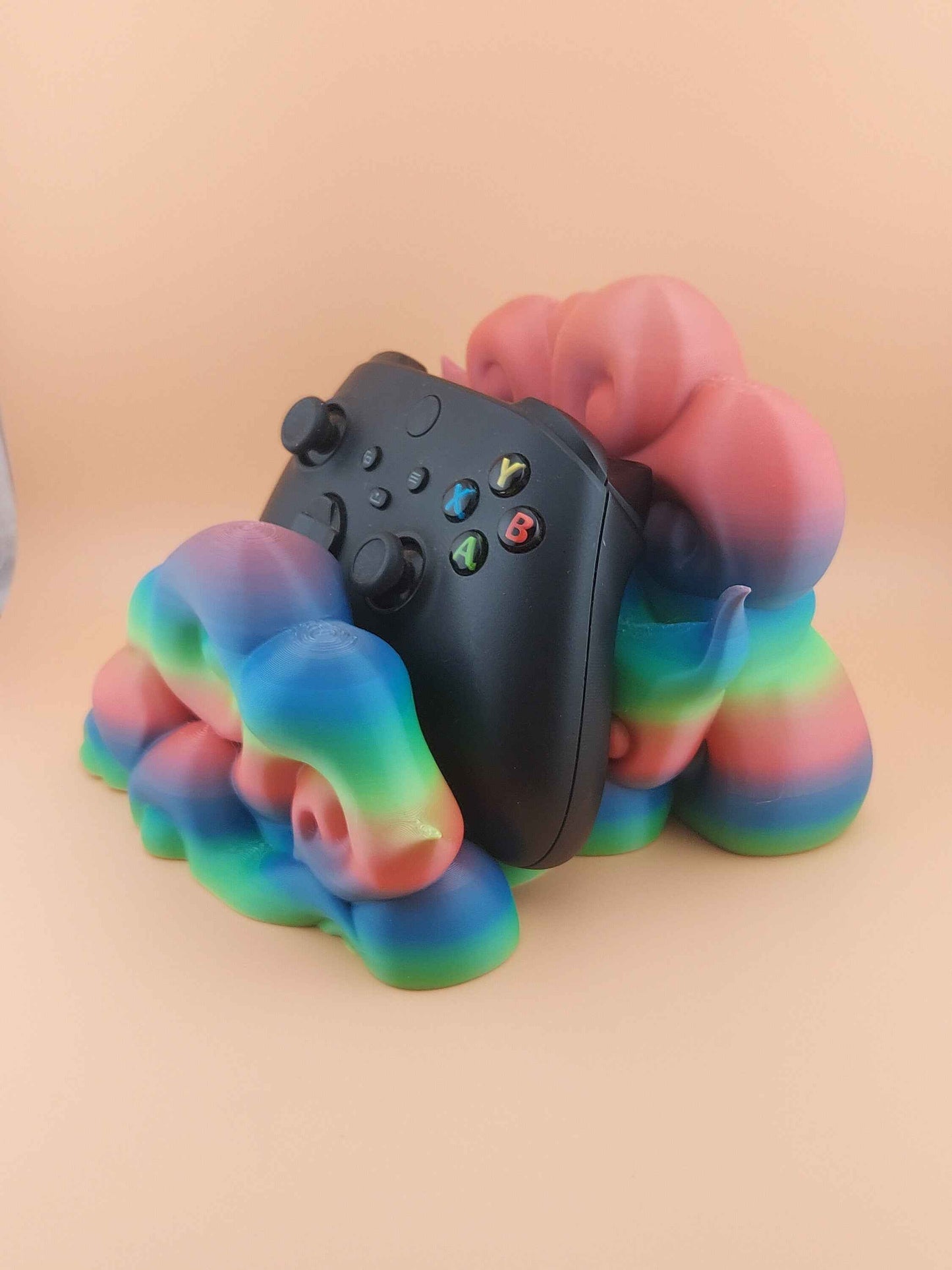 High three-quarter angle of a glossy black controller resting in a complex, smooth, rainbow-gradient plastic stand with sculpted curves.