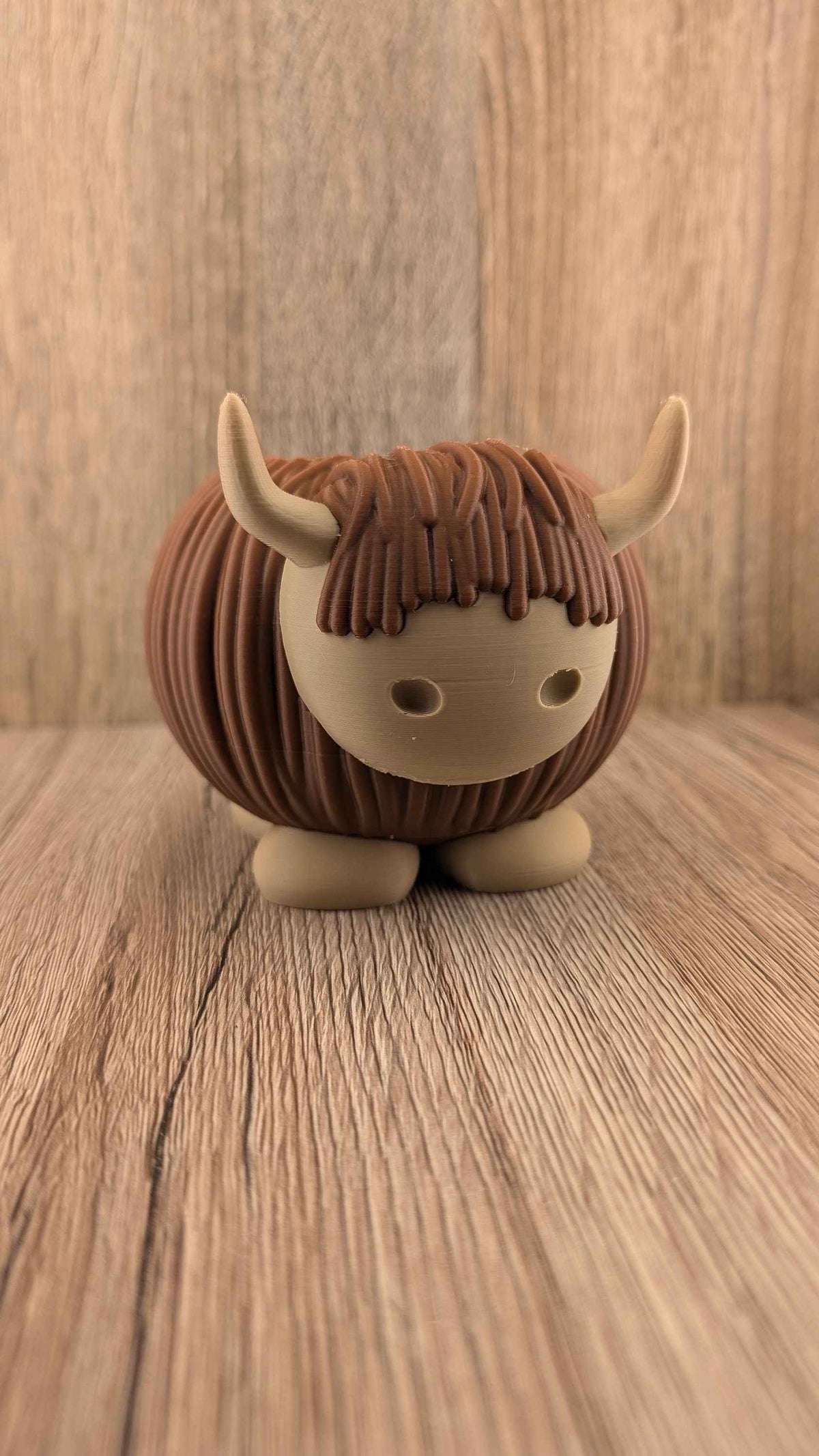 Centered, symmetrical front view of the brown and tan Highland Cow planter on a rustic wooden plank surface.