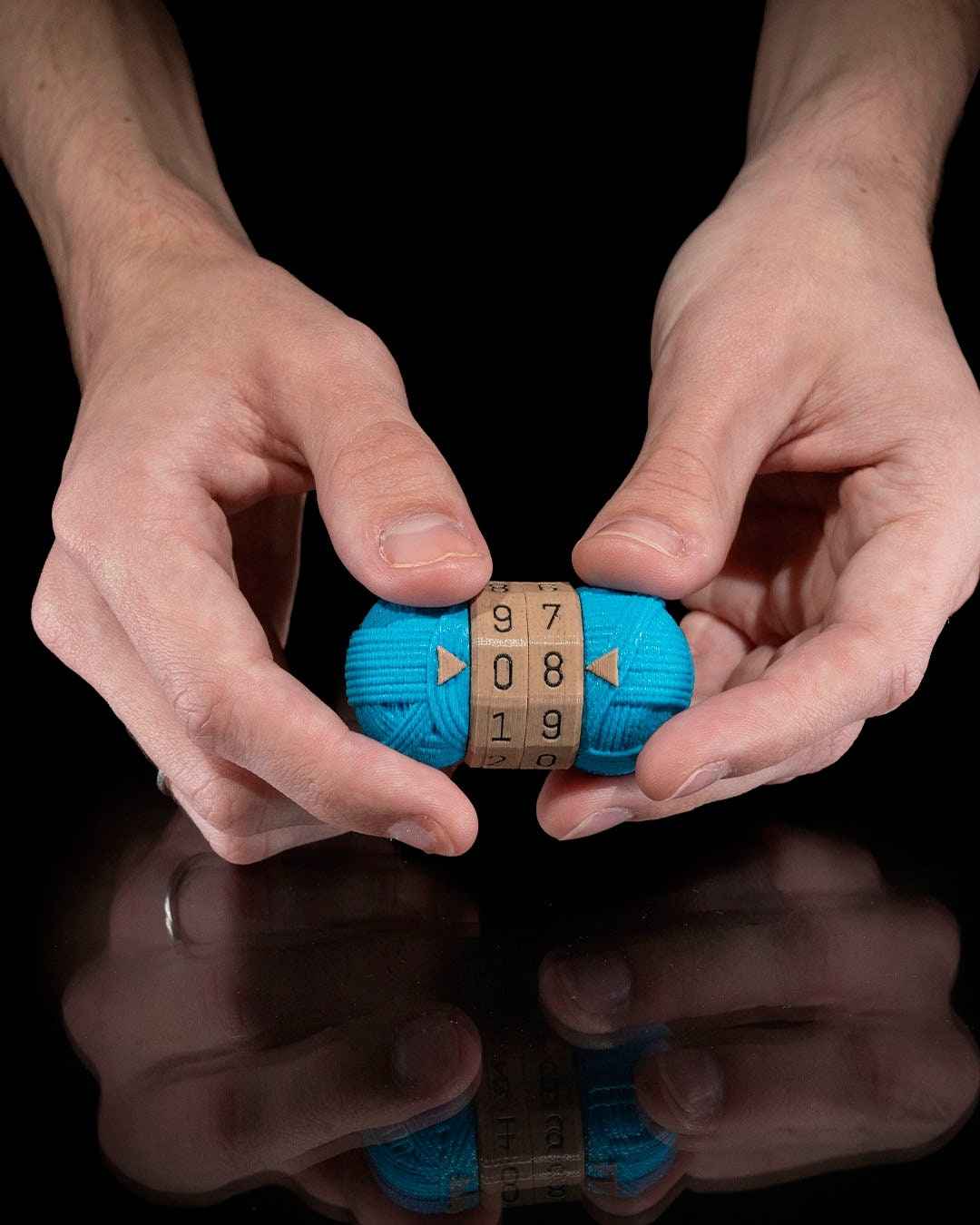 Two hands holding the bright teal yarn counter fidget against a dark backdrop. The central rotating dials read 97, 08, 19.