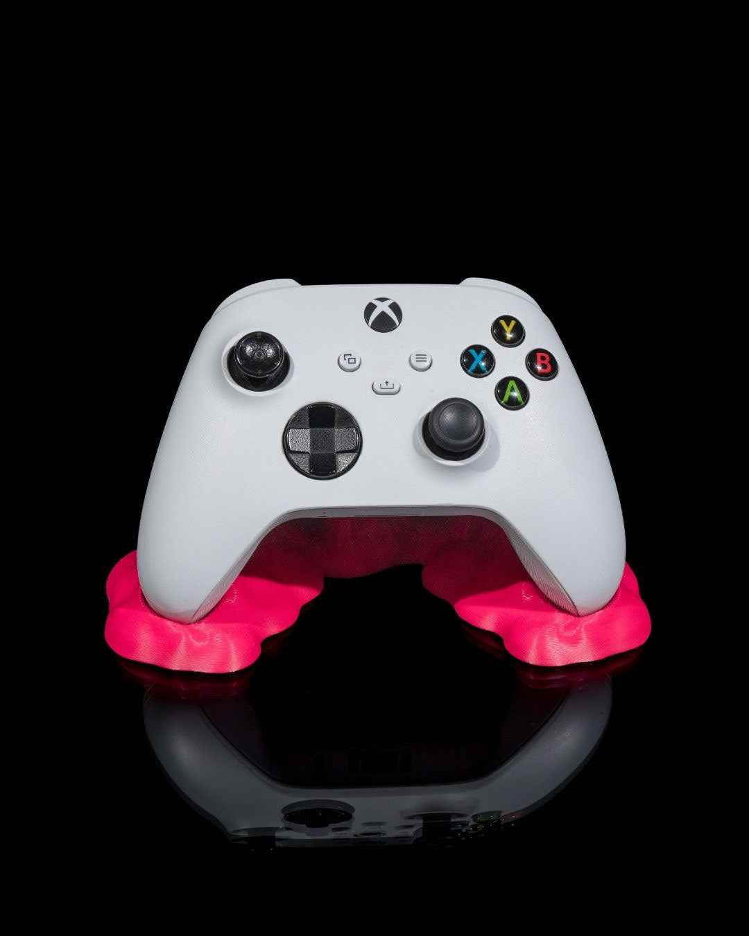White Xbox controller centered on the rounded base of the vivid hot pink melted slime stand. Black background.