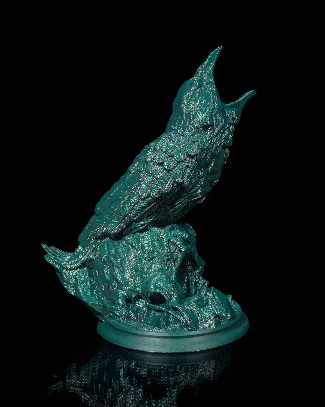 Full view of the highly detailed, shiny deep green raven statue cawing on its skull base. Low angle creates dramatic lighting.