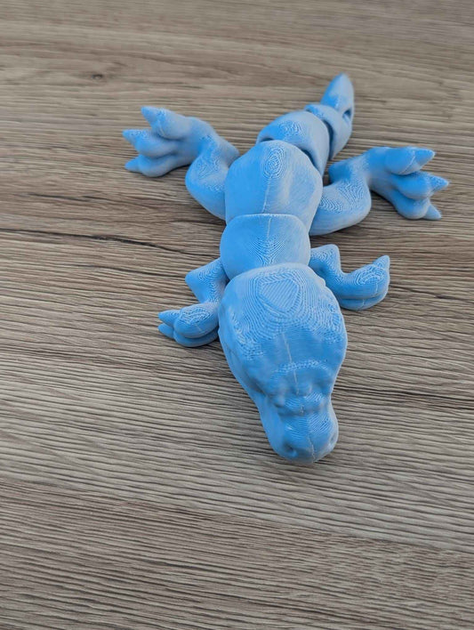 Top-down view of the flexible matte blue dinosaur figurine, highlighting the articulated spine and limbs.