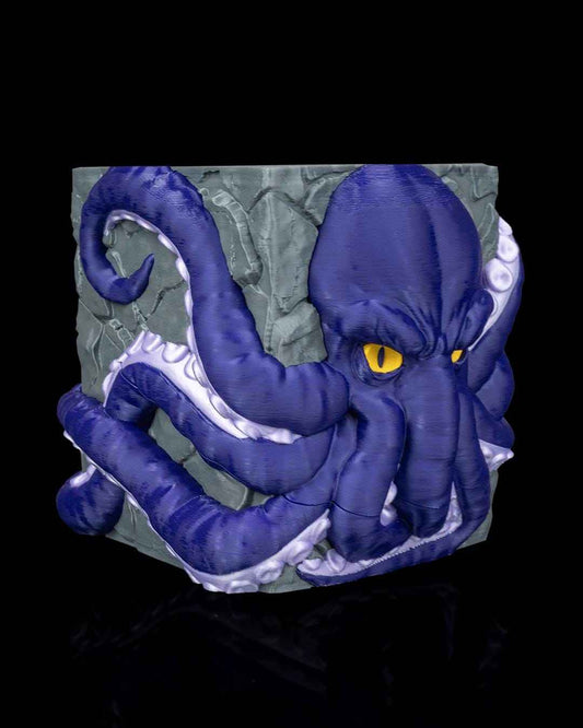 Deep blue octopus head and white-suckered tentacles wrapped around the gray textured stone cube. Slightly angled view.