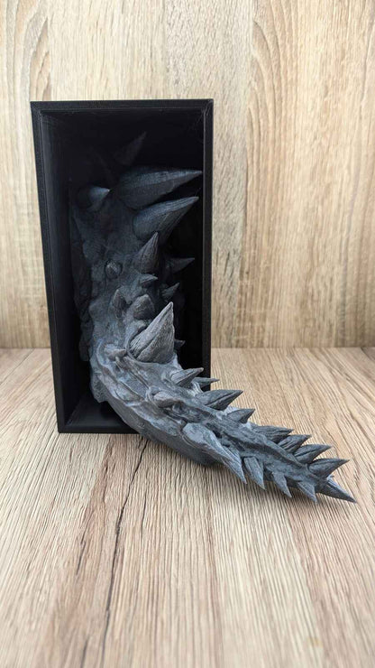 Central view of the textured, spiky dark grey dragon tail extending out and resting on the wooden surface.
