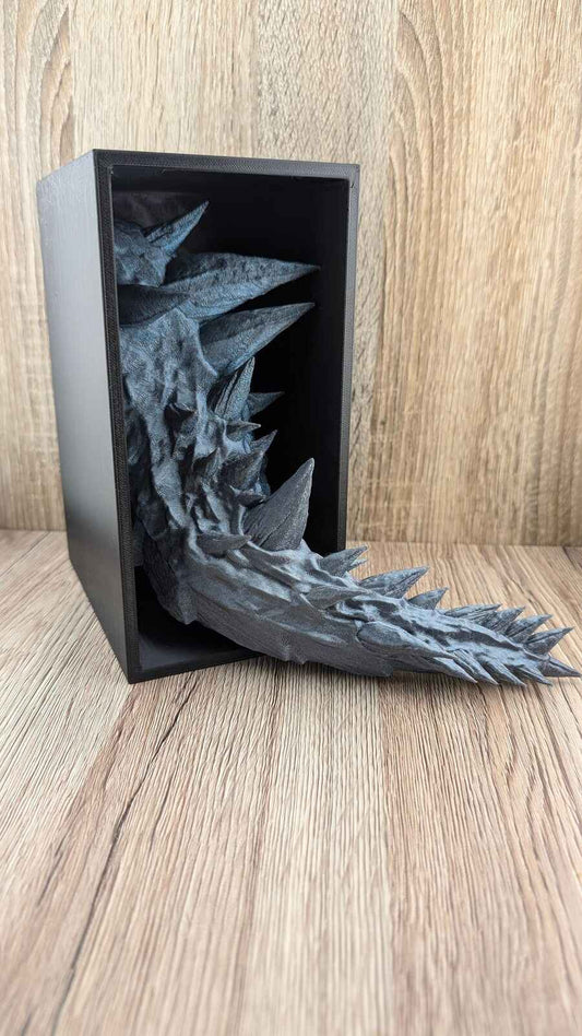 Full shot of the rough slate grey dragon tail sculpture emerging from the dark black box.