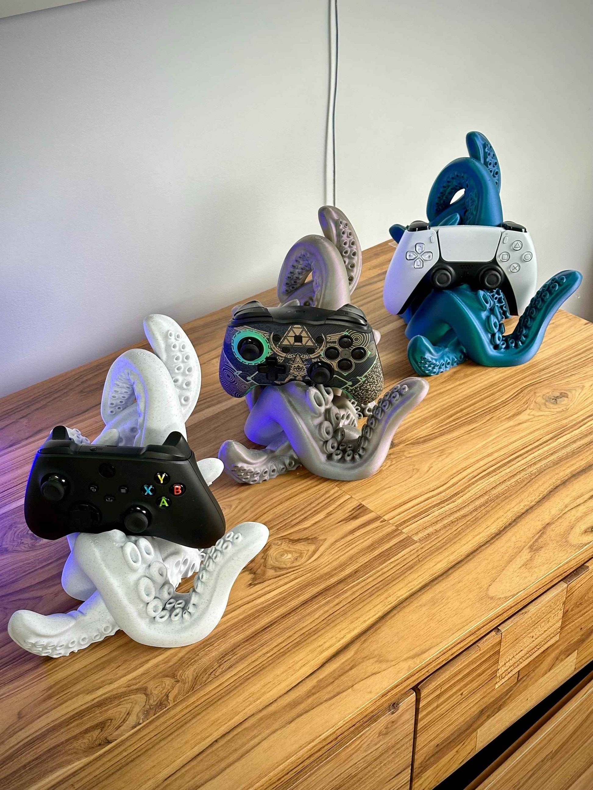 Tentacle controller holder holding a PS5, Switch pro and Xbox controller on a wooden desk.