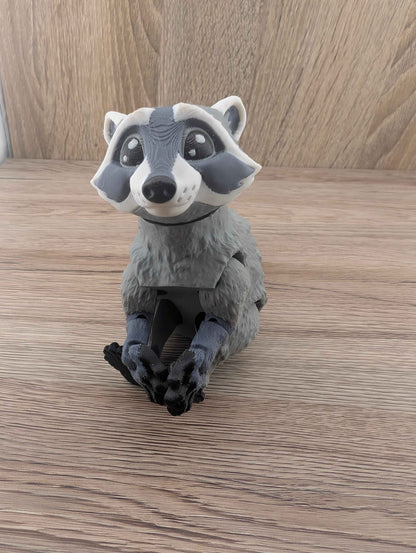 Grey and white articulated raccoon toy figure sitting upright on a wooden floor with its dark paws crossed.