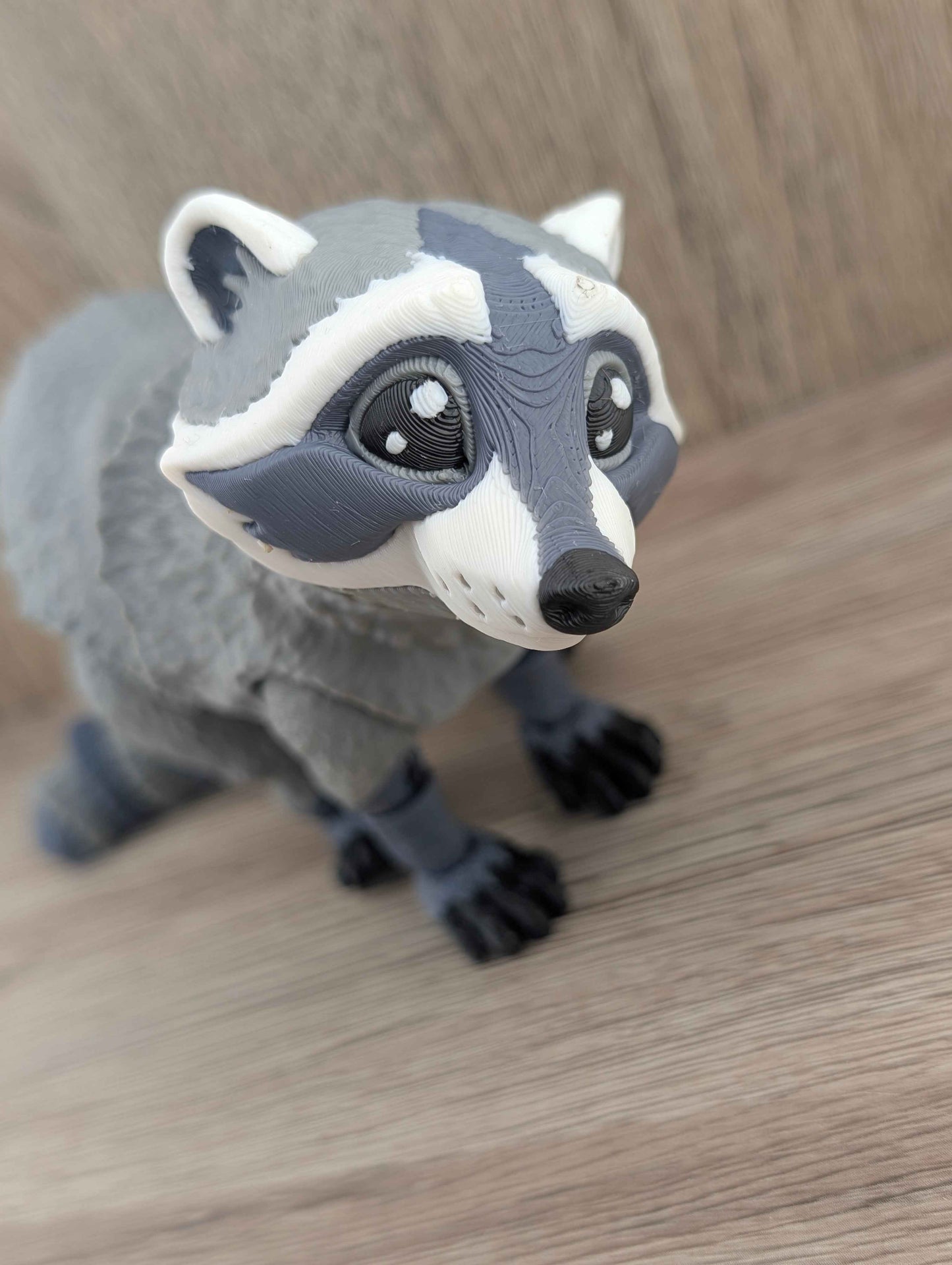 High-angle close-up of the raccoon figurine looking up, highlighting the white and gray striped facial features and dark paws.