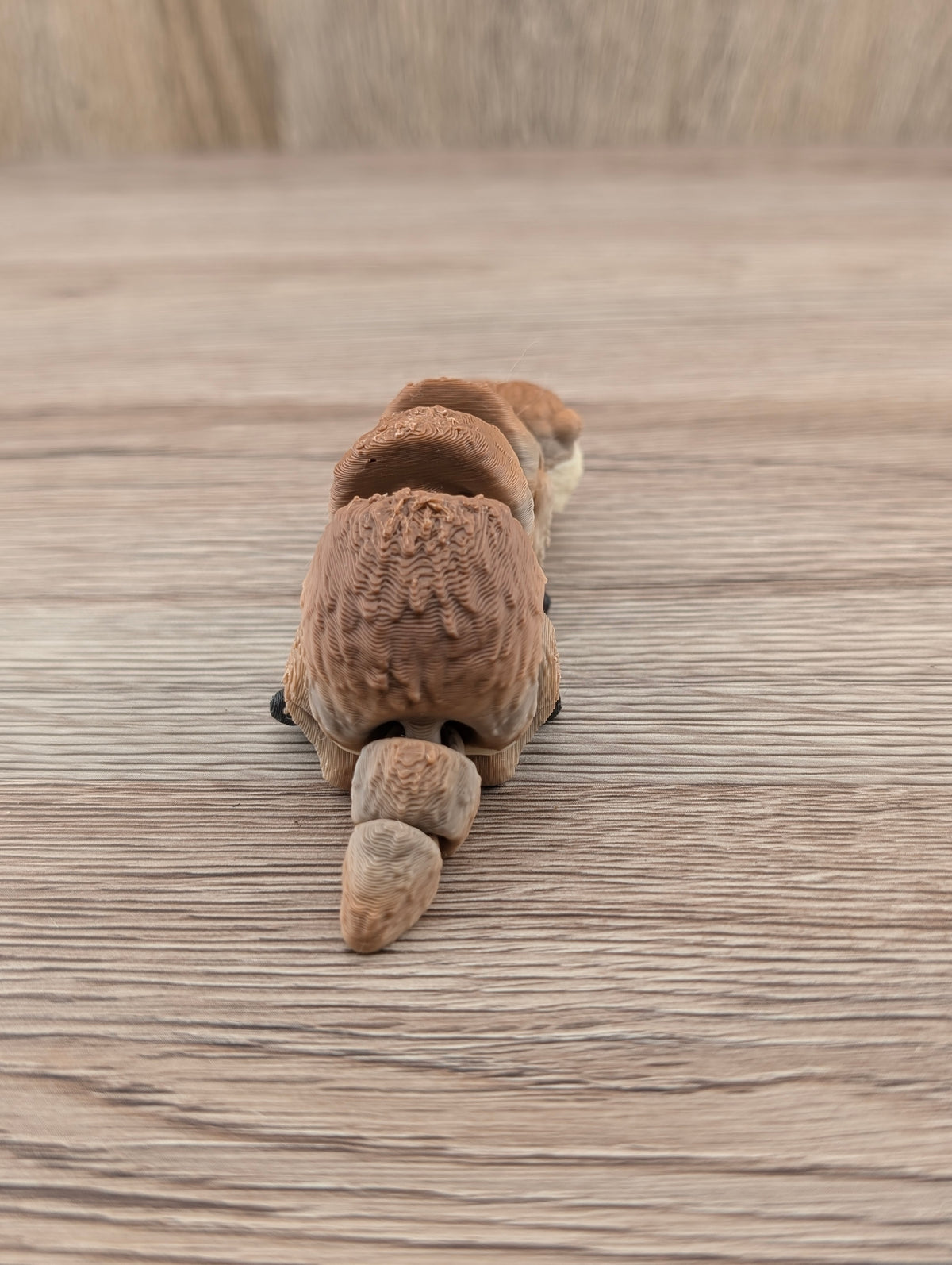 Rear view of the brown segmented toy animal. Detailed layered texture visible across the body and rounded, flexible tail.