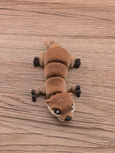 Articulated brown otter toy lying flat on light wood grain; segmented body and textured surface detail visible.