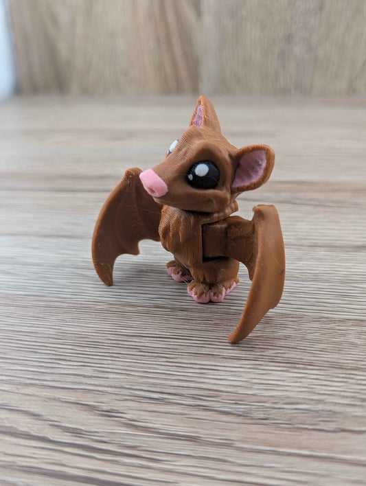 Profile view of the segmented brown bat toy showing its large head, articulated torso, and short, wide wings. Resting on light wood.