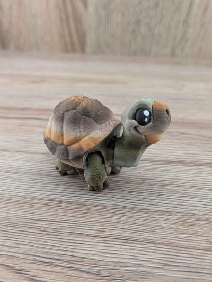 Mini turtle fidget toy with a brown and orange patterned shell, side view on a wooden surface