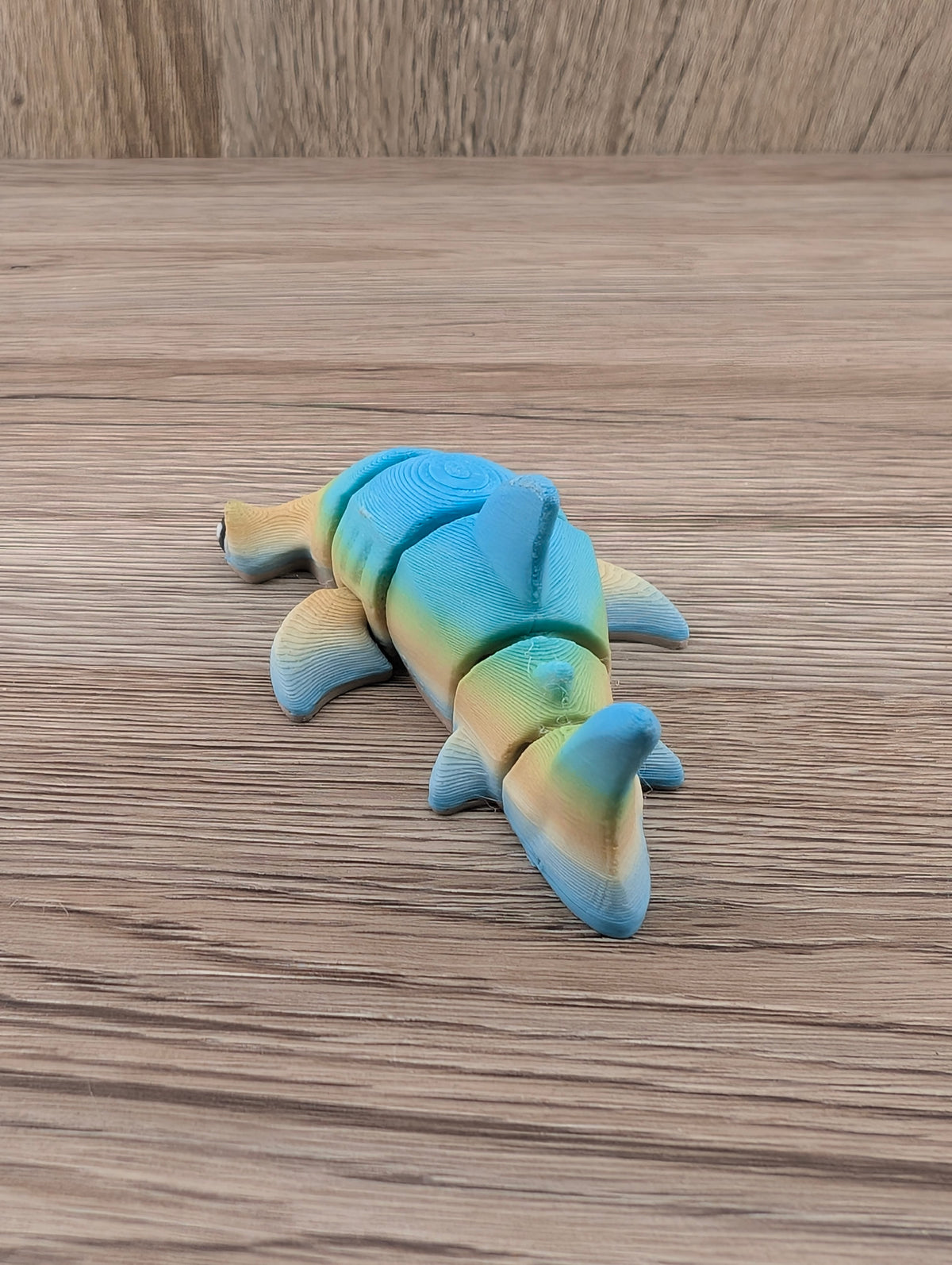 Top-down view of the flexible blue and yellow shark toy, featuring prominent segmented joints and sweeping dorsal fins.