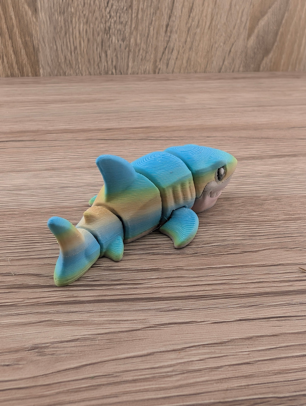 Rear three-quarter view of the flexible blue, yellow, and beige shark toy showing segmented body joints and fins.