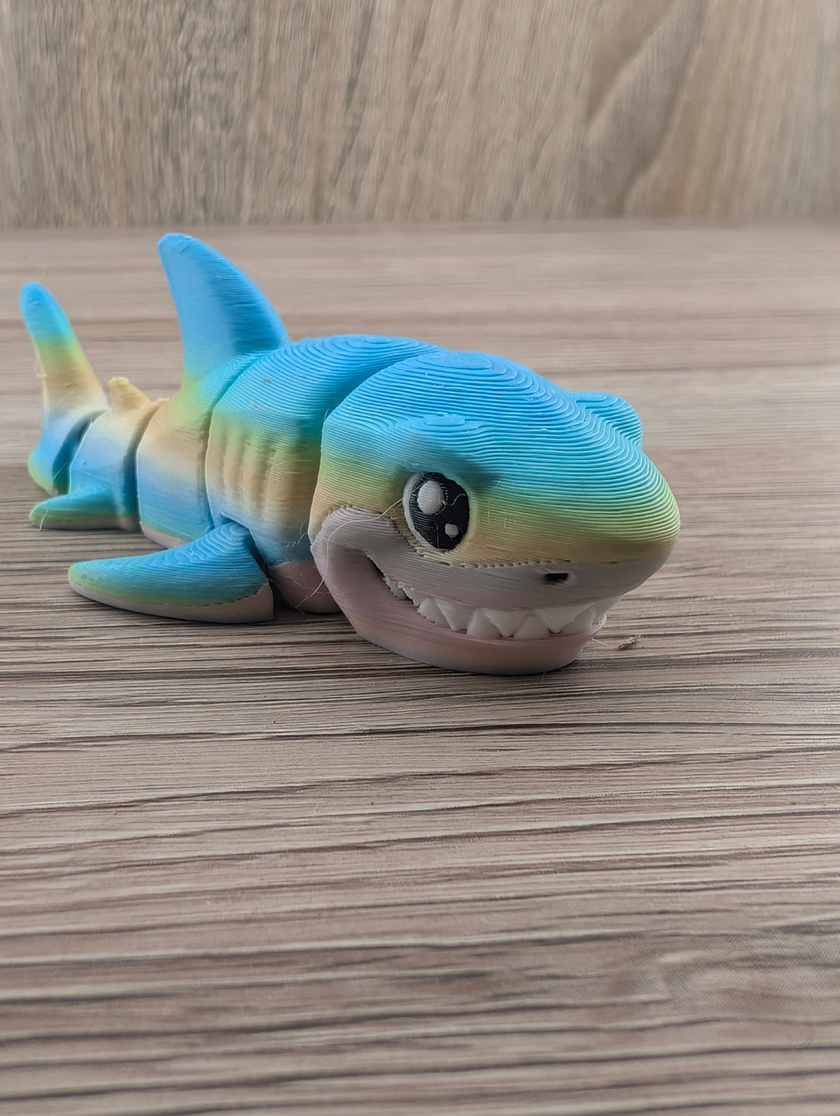 Close-up of the playful, textured shark figure. Large eye and pronounced white teeth visible below the blue body.