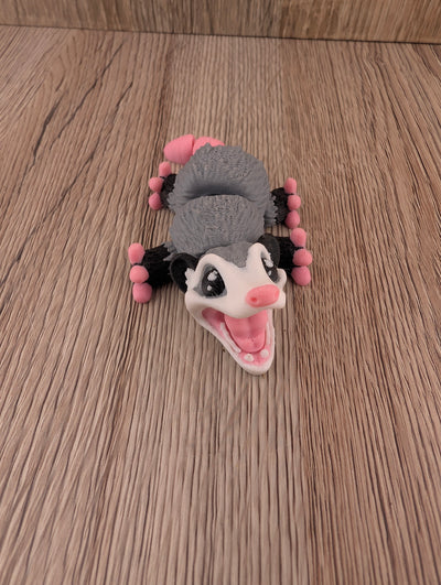 Close-up of the grey and white figurine lying supine on wood, featuring the pink mouth and wide black and white eyes.