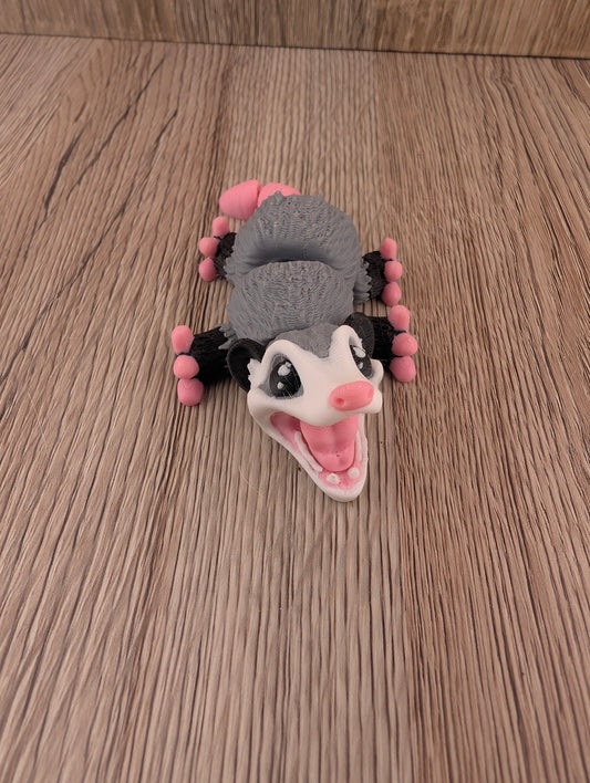 Close-up of the grey and white figurine lying supine on wood, featuring the pink mouth and wide black and white eyes.