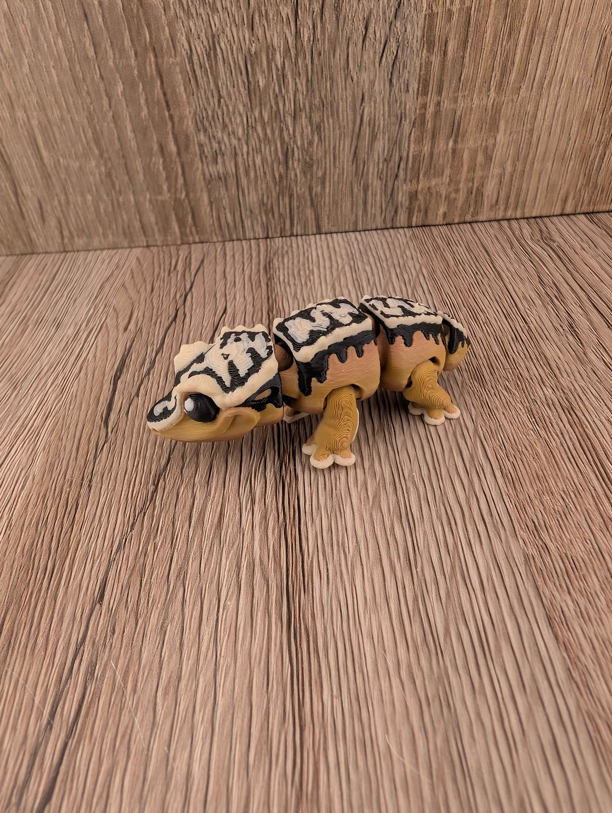 Segmented beige and brown reptile figure with bold black and white markings, posed on a rustic wooden floor texture.