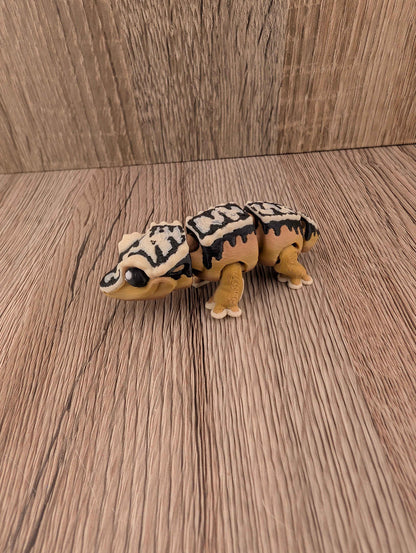 Segmented beige and brown reptile figure with bold black and white markings, posed on a rustic wooden floor texture.