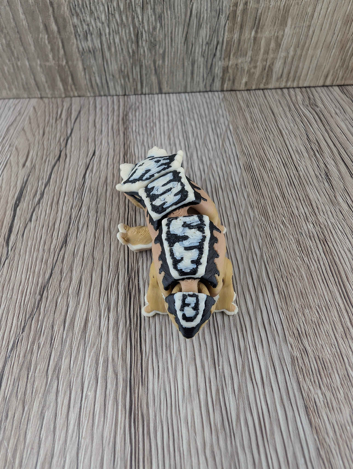 Overhead view of the articulated tan lizard toy displaying its dense black and white patterned dorsal shell segments.