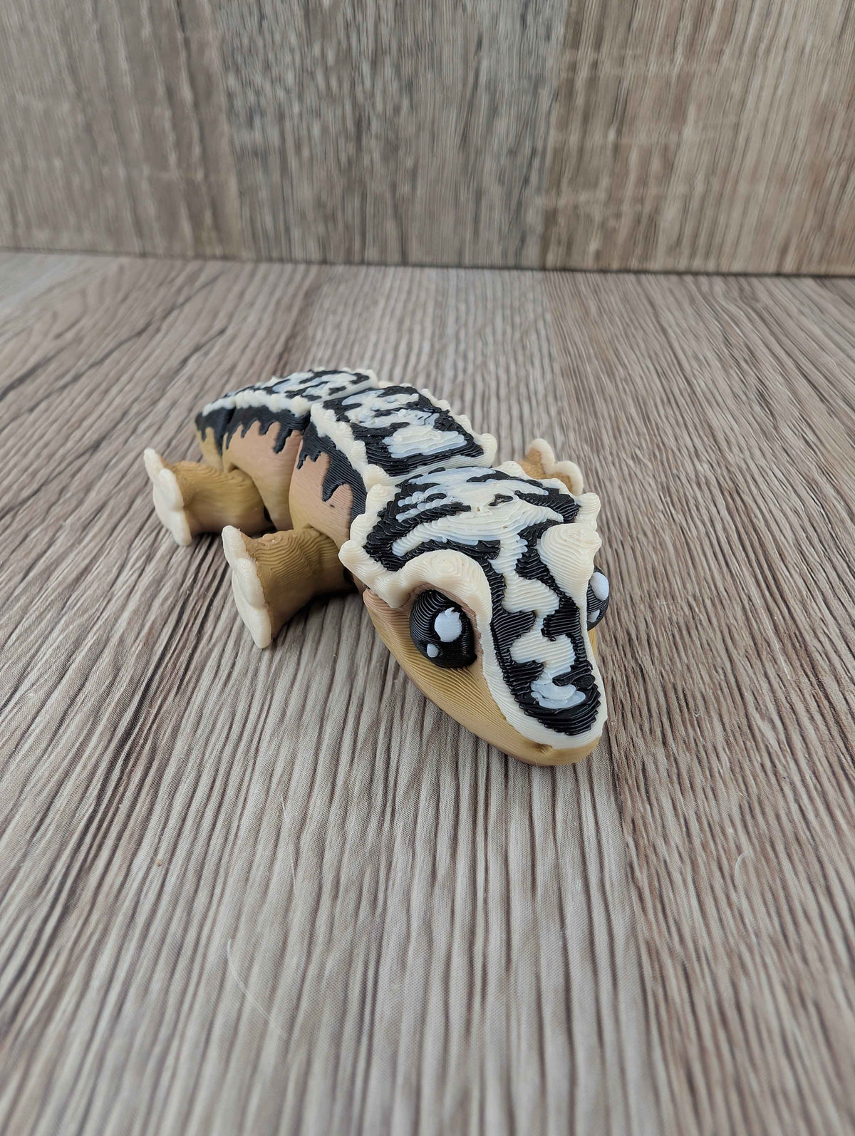 Low angle shot of the articulated gecko toy, showing its beige head, large eyes, and textured black and white spine segments.