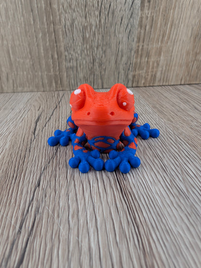 Vibrant red and blue spotted reptile figurine with layered texture, large white eyes, posed on rustic wood.