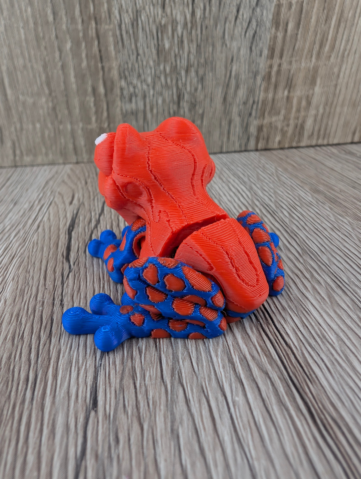 Back view of the plastic spotted frog figurine. The rear legs have a vibrant blue base with many orange round spots.