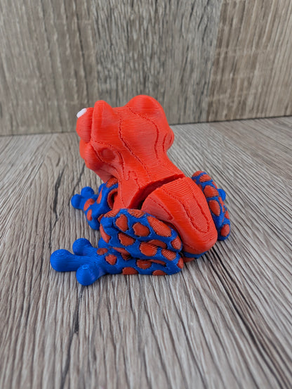 Back view of the plastic spotted frog figurine. The rear legs have a vibrant blue base with many orange round spots.