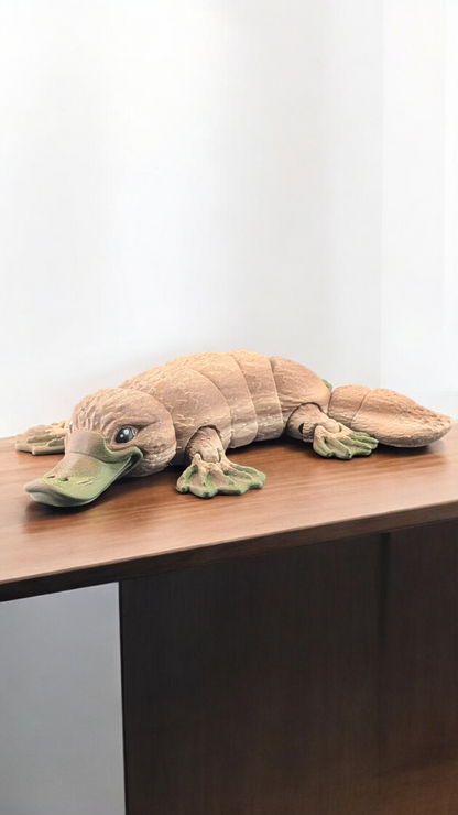 Side view of the articulated tan platypus toy lying flat on a desk, showcasing its full segmented length.