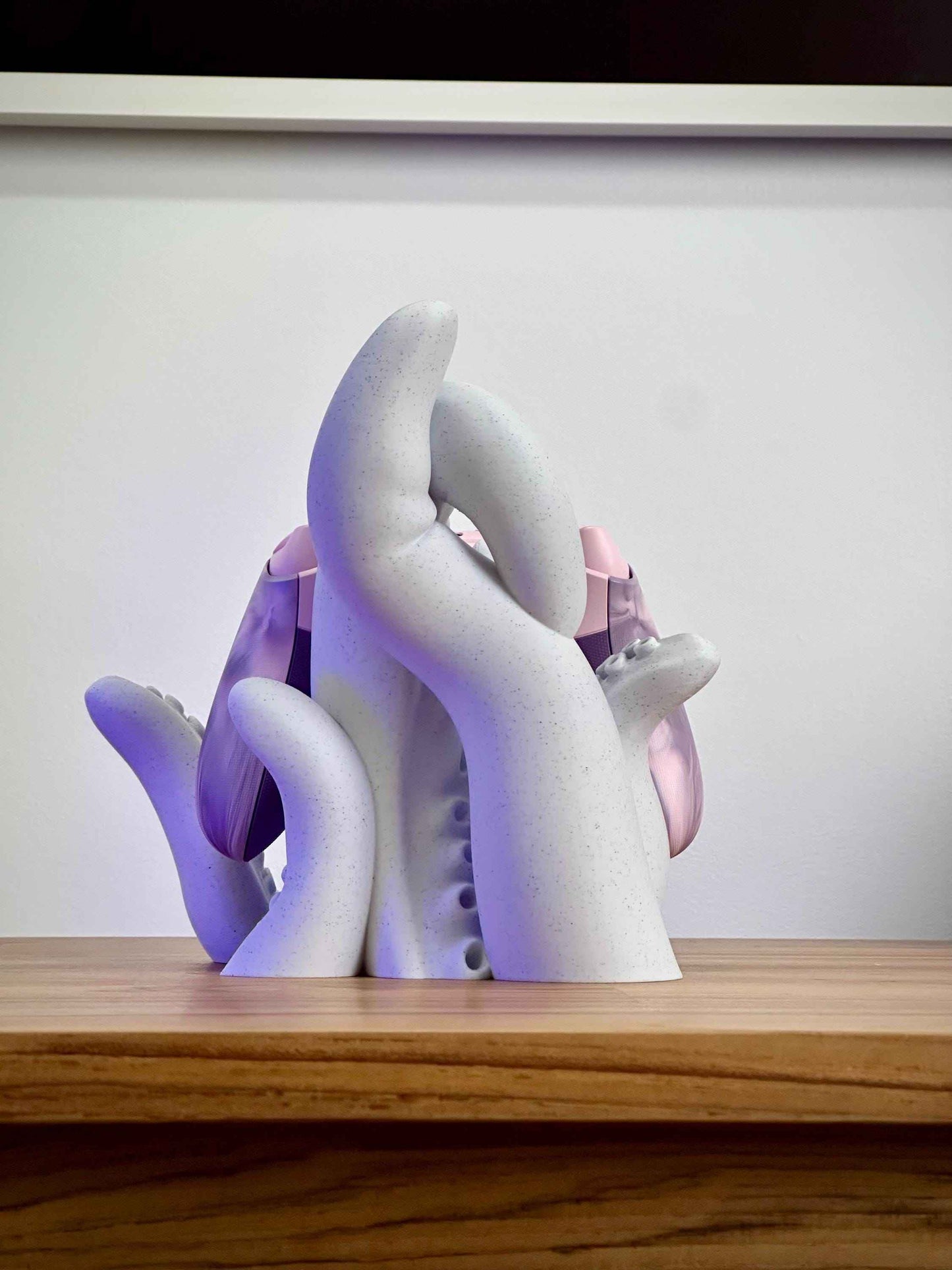 Marble tentacle controller holder from the back holding a pink Xbox controller on a wooden desk.