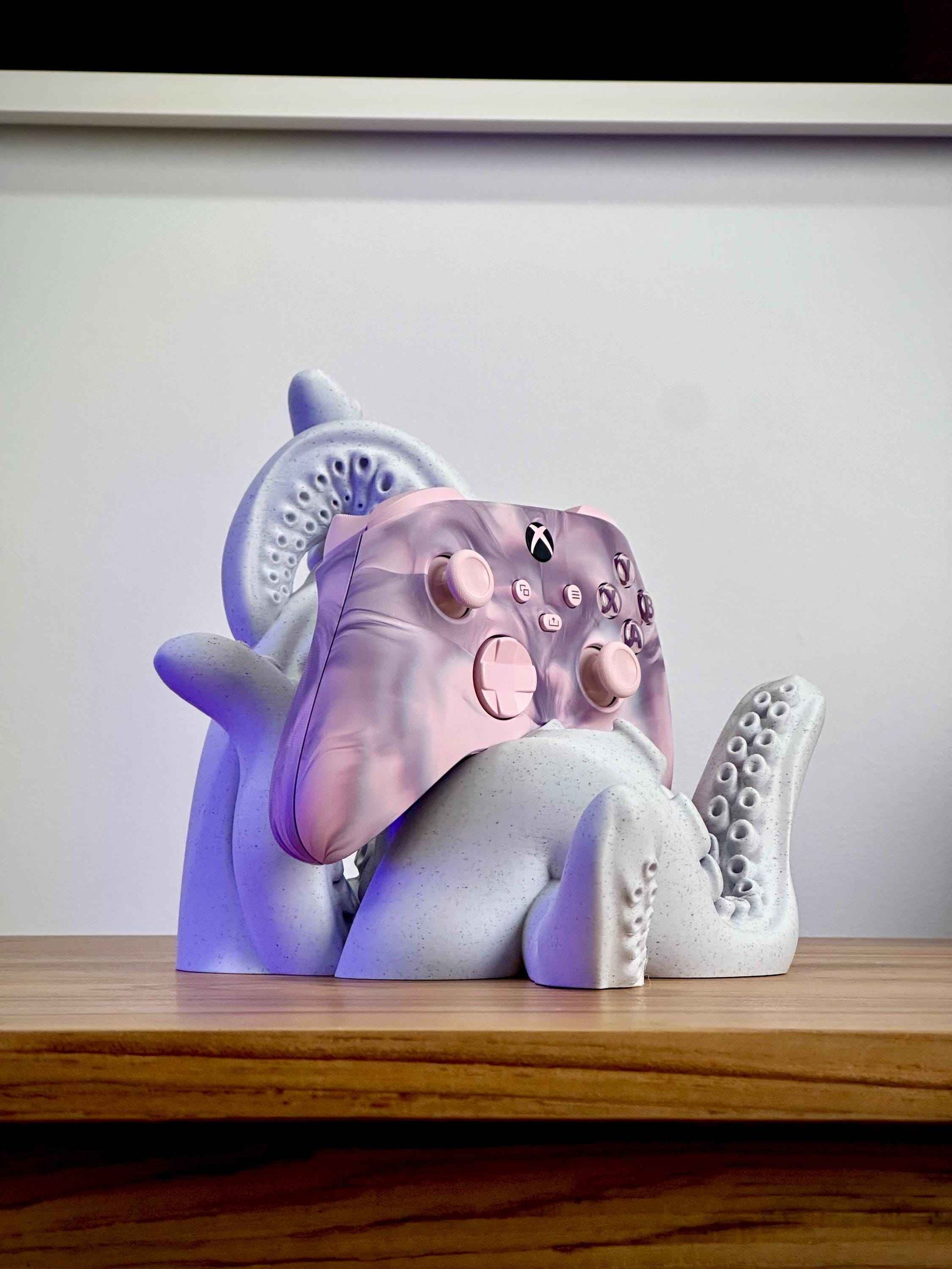 Marble tentacle controller holder holding a pink Xbox controller on a wooden desk.