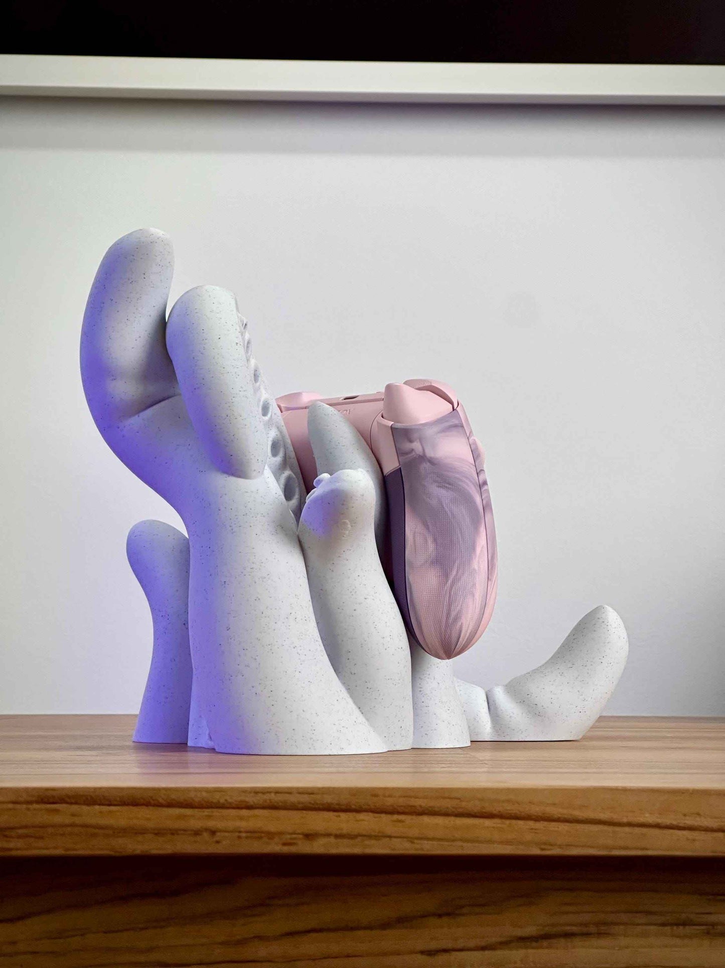 Marble tentacle controller holder from the Back Side holding a pink Xbox controller on a wooden desk.