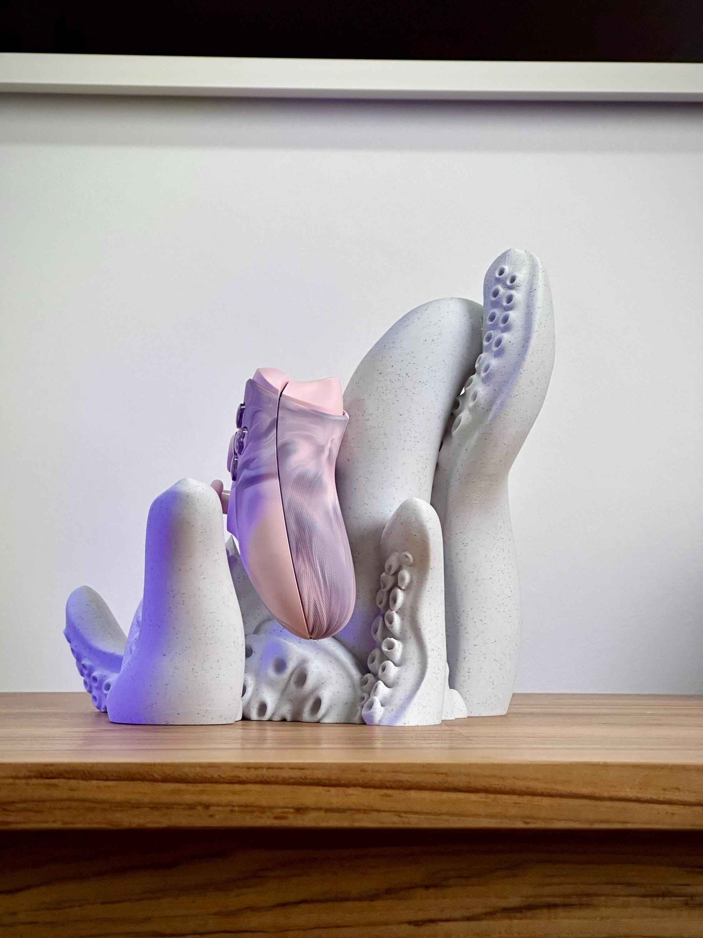 Marble tentacle controller holder from the Side holding a pink Xbox controller on a wooden desk.