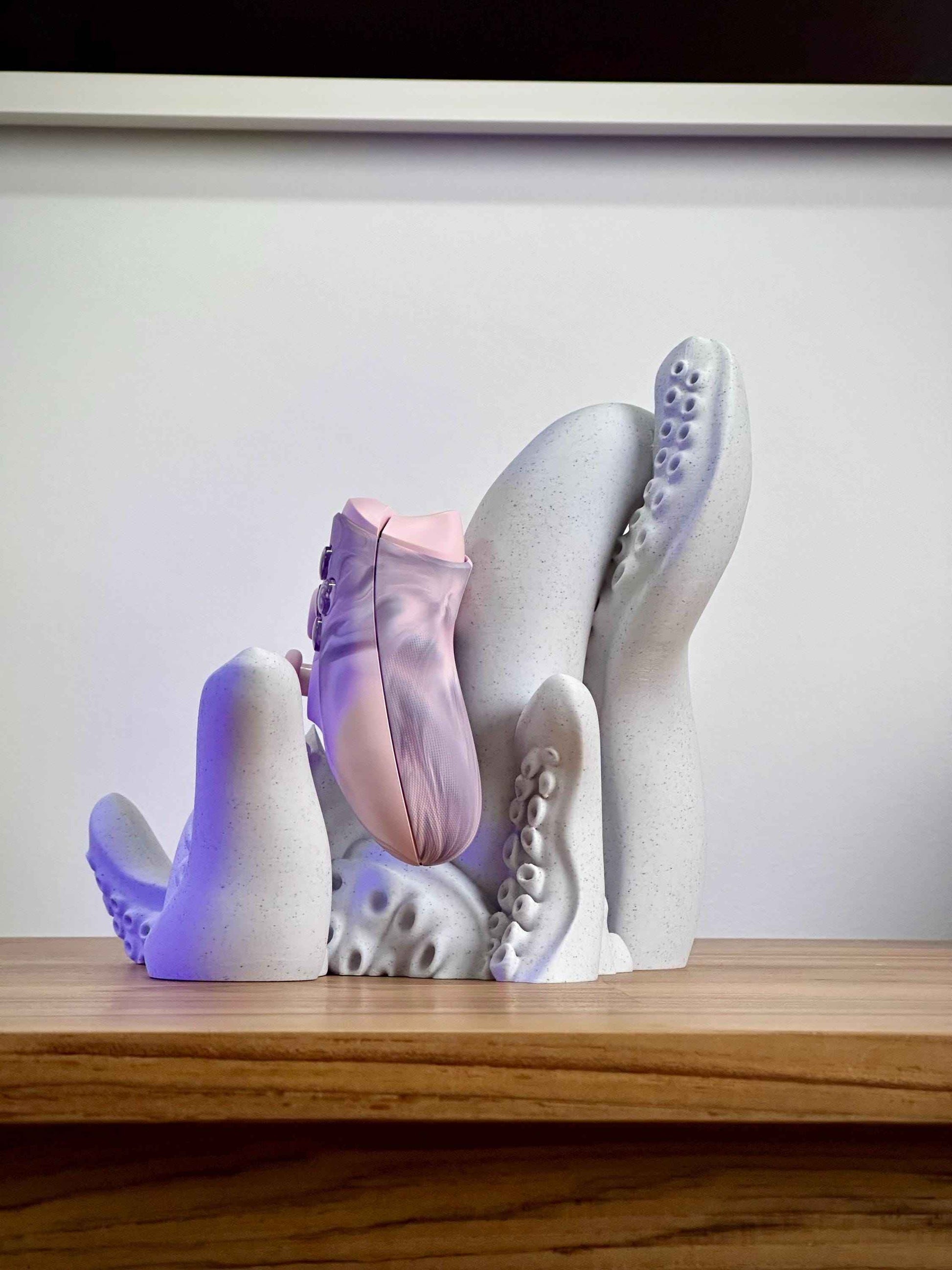 Marble tentacle controller holder from the Side holding a pink Xbox controller on a wooden desk.