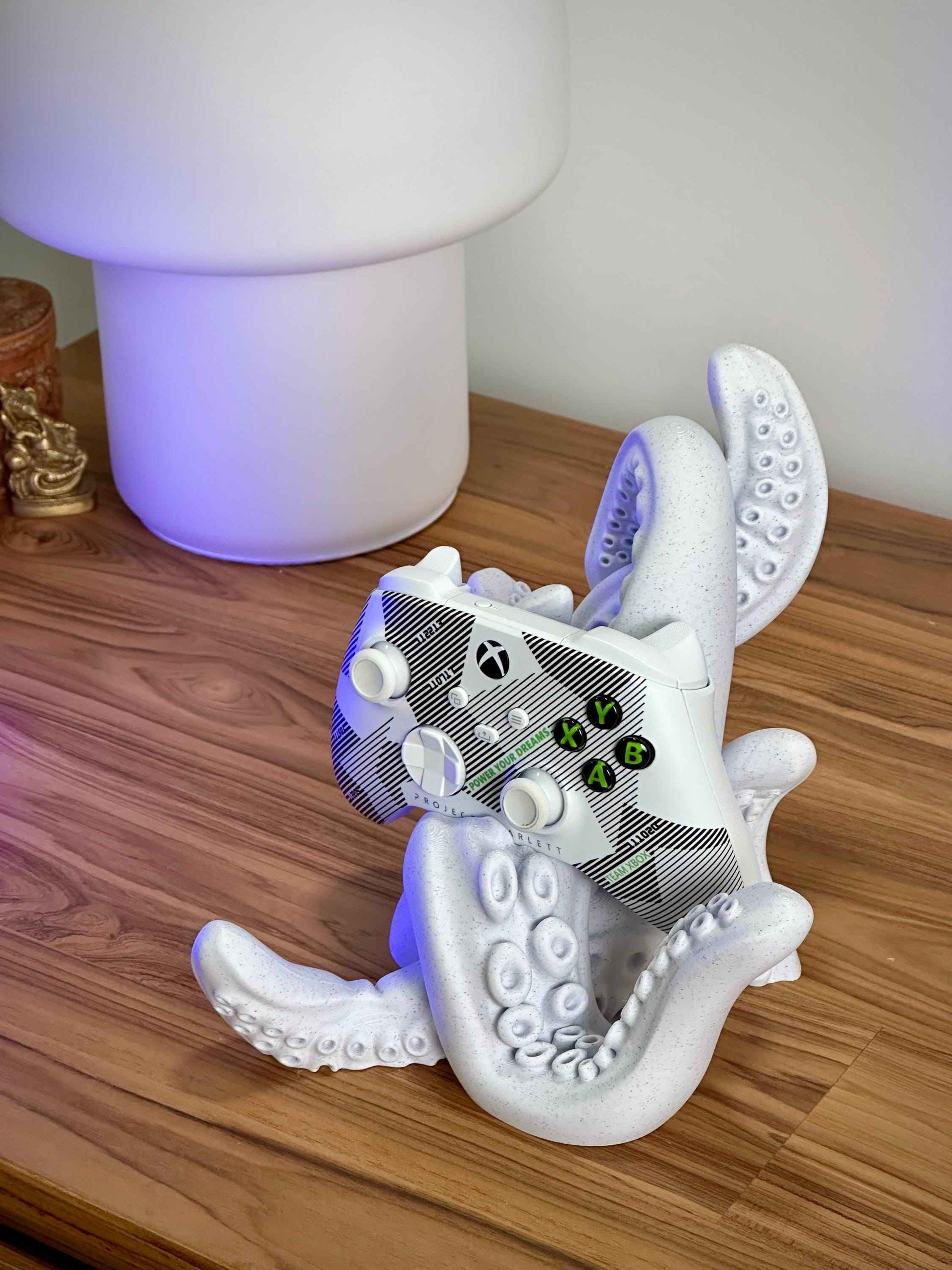 Marble tentacle controller holder holding a white Xbox controller on a wooden desk.
