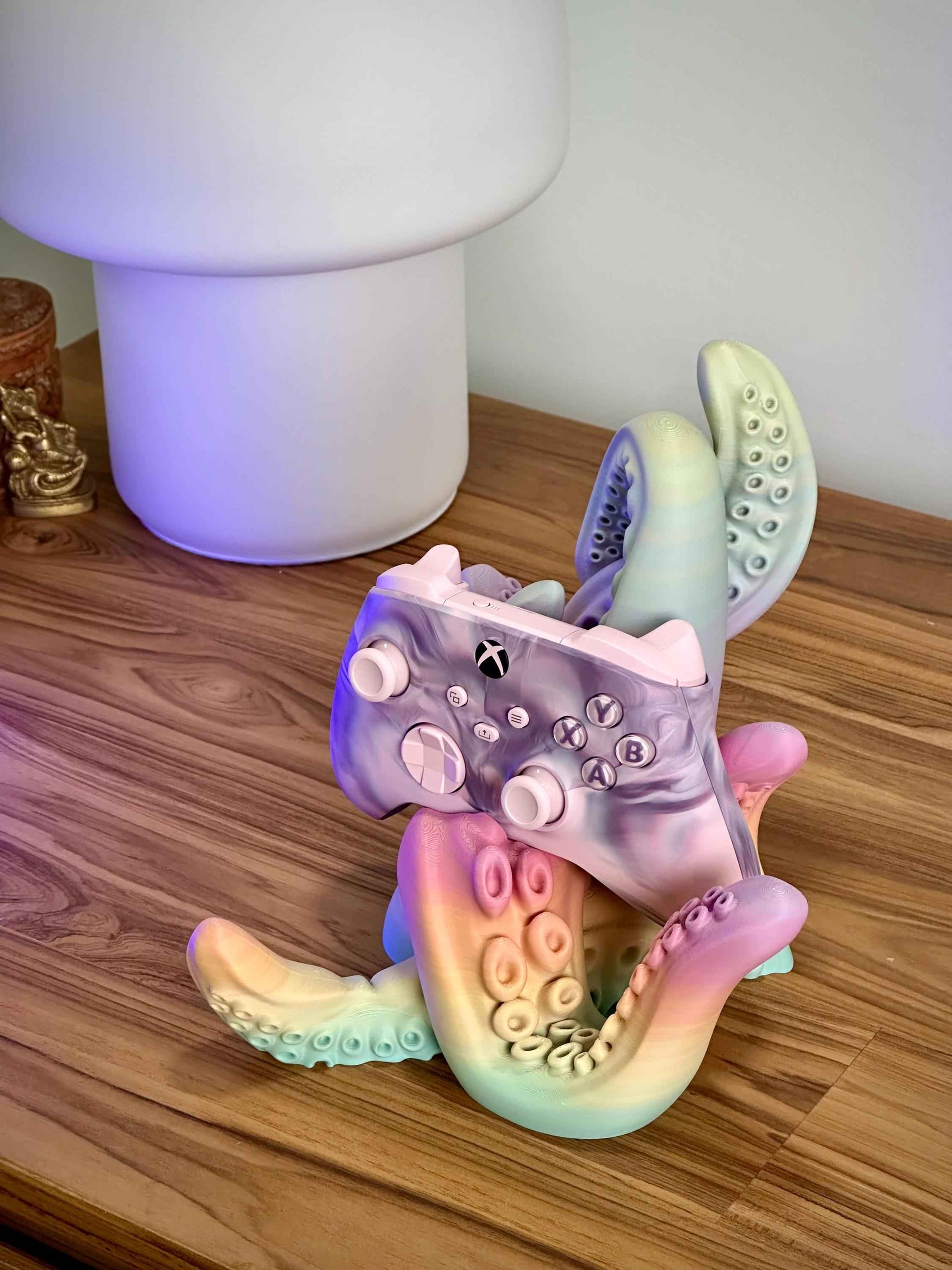 Matte Rainbow tentacle controller holder holding a Pink PS5 controller on a wooden desk.