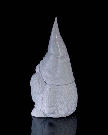 Side profile view of a stout gnome statue with a long tapered cap, finished in a matte, speckled grey stone texture.