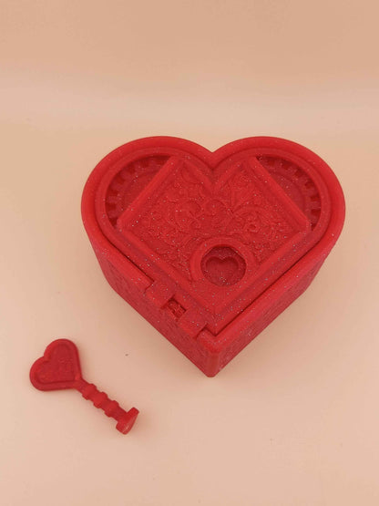 Closed sparkly red heart lockbox, featuring engraved filigree on the lid. The matching heart key rests below it.