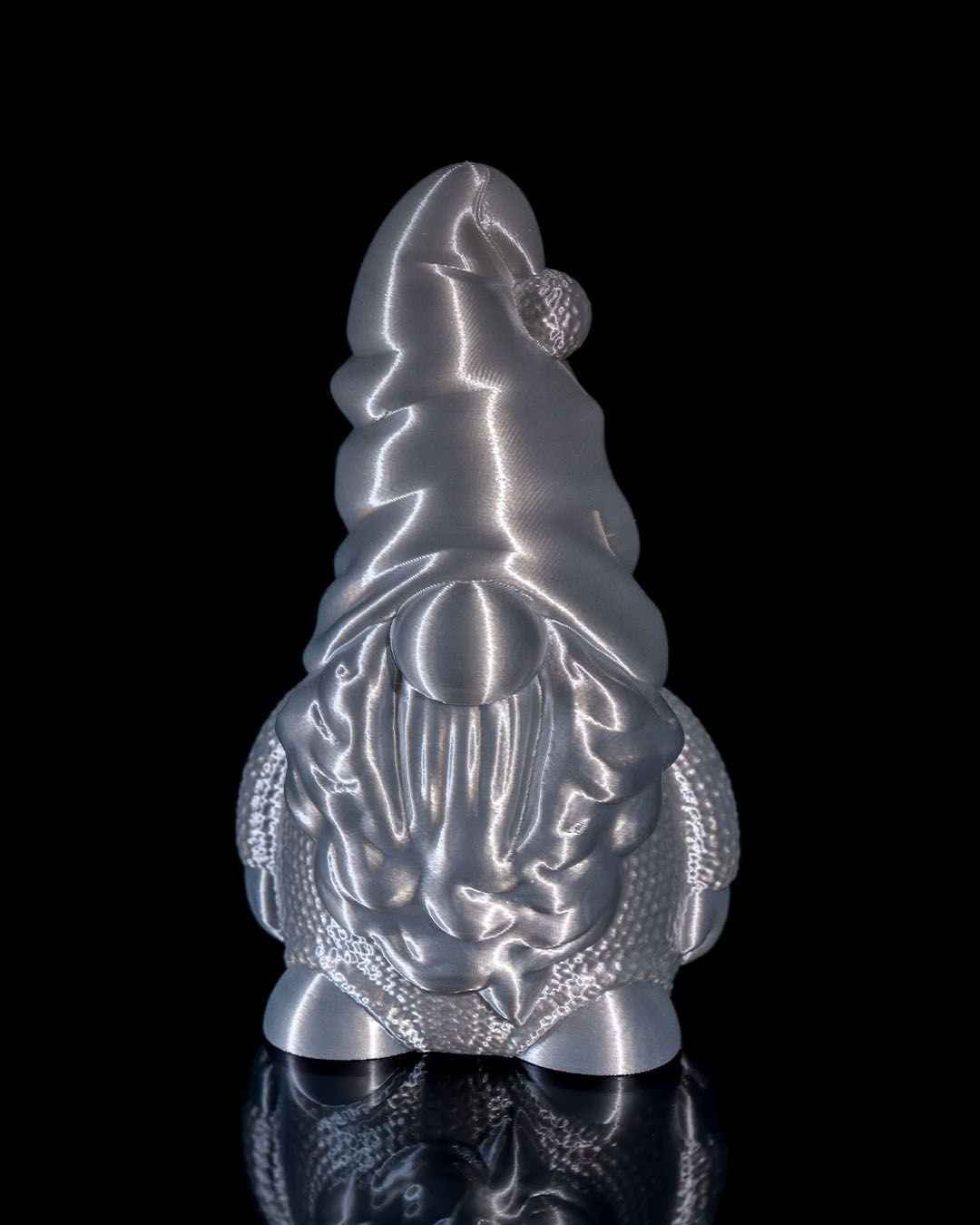 Front profile of a festive gnome figure with a pom-pom hat texture, highly reflective chrome metallic silver finish.