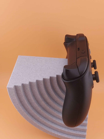 Black controller side profile resting on the high speckled grey stand, positioned where the curved steps meet the flat top.