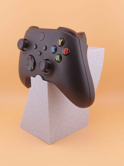 Low-angle three-quarter view of the black controller displaying face buttons, held by the short grey stepped stand.