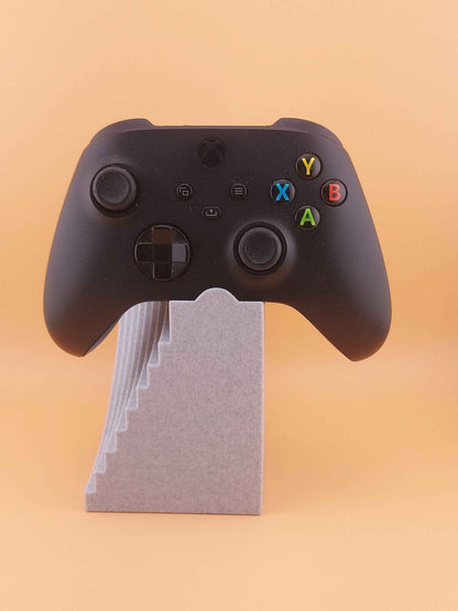 Straight-on view of the black controller showing all face buttons, elevated slightly by the speckled grey stepped stand.