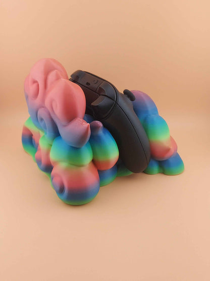 Three-quarter view of a black controller resting steeply in a smooth, rounded, multicoloured gradient plastic cloud stand.