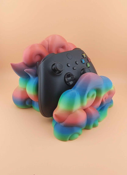 Straight view of a black controller resting in a  glossy, rainbow-gradient plastic cloud holder against a beige background.