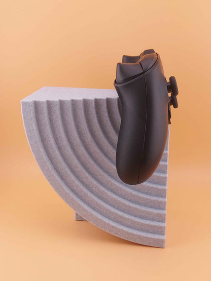 Matte black game controller side profile resting on the speckled grey stand featuring deep curved ridges.
