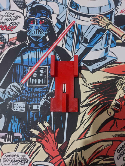 Matte red T-shaped bracket rests flat on the vivid Star Wars wallpaper, showing the keyhole attachment slot.